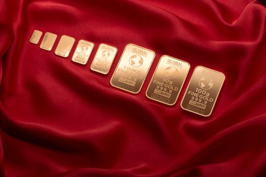 Goudbaren en munten naast een rekenmachine en koersgrafiek over nu beleggen in goud